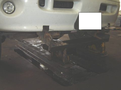 1992 Ford Bronco - White SUV front end is raised on a lift in a garage.