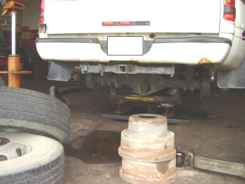 1992 Ford Bronco - The rear of a white truck is shown, with its undercarriage and tow hitch visible. The vehicle appears to be in a repair shop.