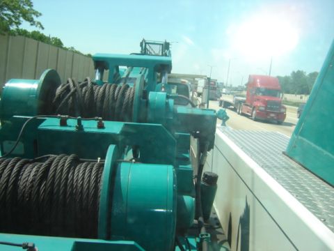 1992 Ford Bronco - Large winch mechanism on a flatbed truck, with other vehicles on the highway.