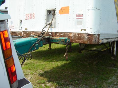 1992 Ford Bronco - A white trailer is connected to a teal trailer hitch, with visible rust on the trailer's frame.