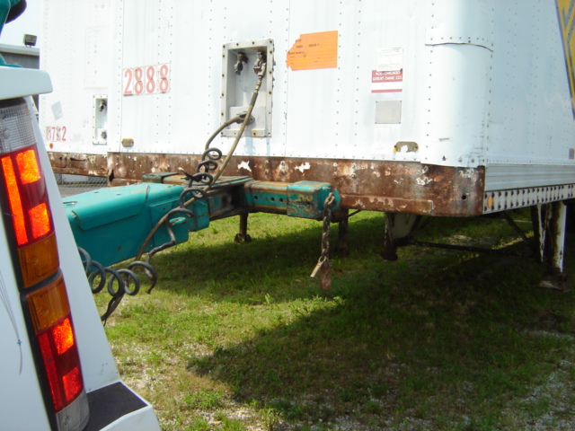 White trailer with rusty undercarriage and teal trailer hitch, viewed from the rear