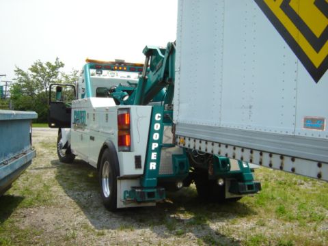 1992 Ford Bronco - A tow truck is attached to the rear of a large trailer, with the truck's name 'Cooper' visible on its side.