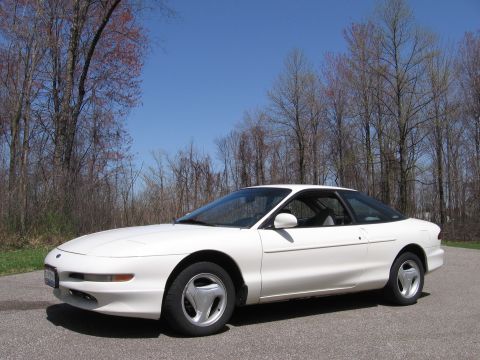 1997 Ford Probe - A white 1997 Ford Probe is parked on a road with trees in the background under a clear blue sky.