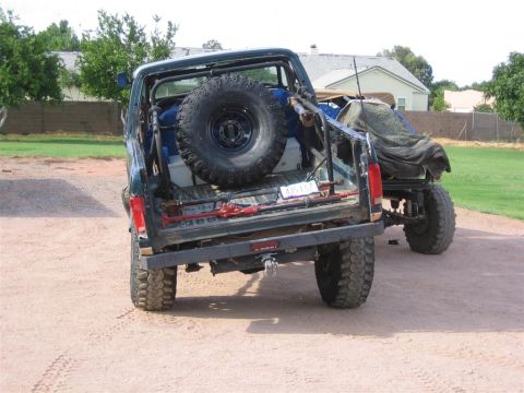 1994 Ford Bronco - Two SUVs are parked on a dirt lot, one with a spare tire and off-road modifications.