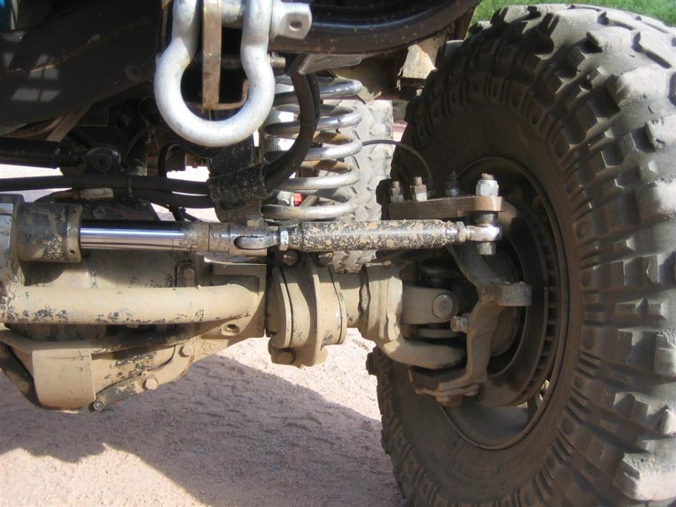 Off-road vehicle's front suspension, steering linkage, and tire with visible "SUPERMOTORS.NET" watermark