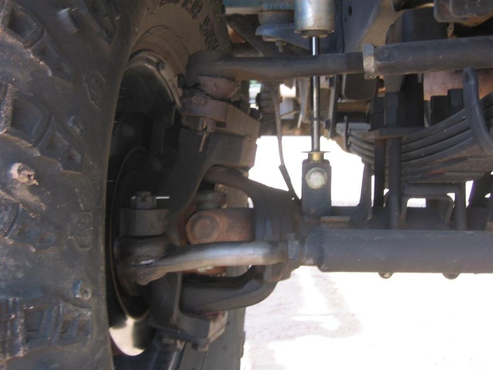 Close-up of a large tire, steering linkage, and leaf springs on a 4x4 vehicle's front suspension