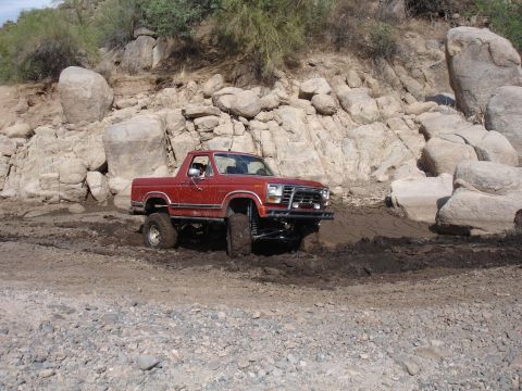 1984 Ford Bronco - This red 1980s Ford Bronco is stuck in mud while navigating a rocky, off-road terrain.