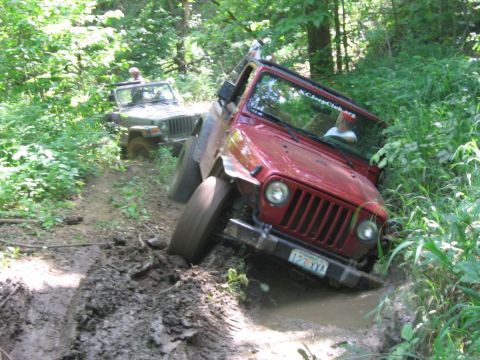 1998 Jeep TJ - Two Jeeps tackle a challenging muddy off-road course, with the lead vehicle partially submerged in mud.