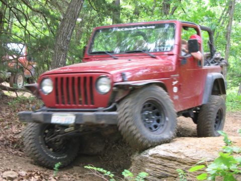 1998 Jeep TJ - A red Jeep Wrangler navigates a rocky trail, with another vehicle partially visible behind it.