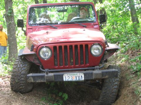 1998 Jeep TJ - Red Jeep Wrangler navigating an off-road trail with large tires and a driver visible.