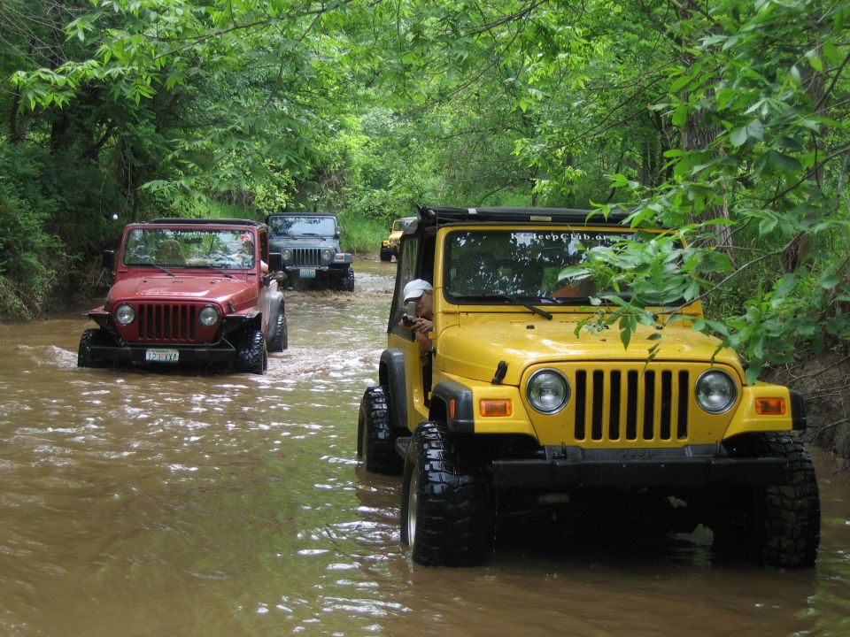 Yellow Jeep TJ front view driving in water, red Jeep TJ and gray Jeep Wrangler behind it