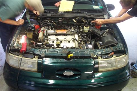1995 Ford Taurus - Mechanics work on the engine of a 1995 Ford Taurus, with the hood open and tools visible.