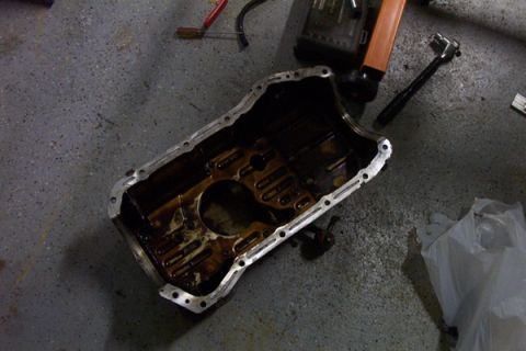 1995 Ford Taurus - A dirty oil pan sits on a concrete floor, surrounded by tools, suggesting an engine maintenance or repair task.