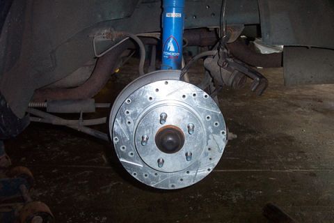 1995 Ford Taurus - Close-up of a car's rear suspension and brake assembly, showing a drilled rotor and a blue Tokico shock.