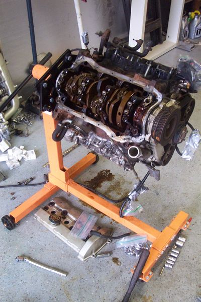 1995 Ford Taurus - Engine disassembled on an engine stand, with various parts and tools on the floor.