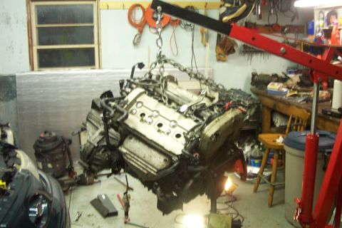 1995 Ford Taurus - An engine is suspended by a red engine hoist in a cluttered garage setting.