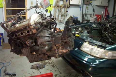 1995 Ford Taurus - Engine removal in progress for a 1995 Ford Taurus, showing the vehicle's engine bay and the detached engine.