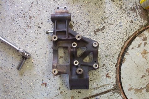 1995 Ford Taurus - A metal engine bracket lies on a garage floor next to a socket wrench, suggesting a repair or replacement in progress.
