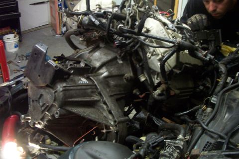 1995 Ford Taurus - A person works on a disassembled engine and transmission assembly in a garage setting.