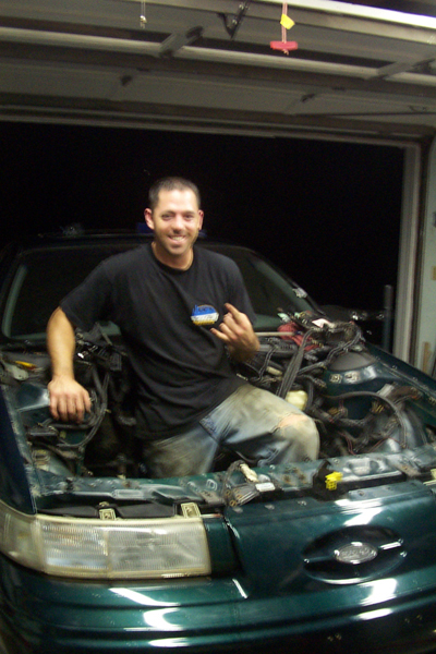 1995 Ford Taurus - Man poses in the engine bay of a 1995 Ford Taurus during an engine refresh or swap.