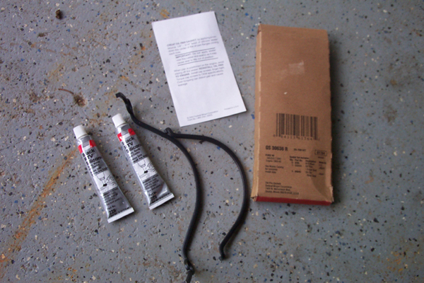 Two tubes of sealant, a black rubber hose, a folded instruction sheet, and a boxed part sit on a concrete floor