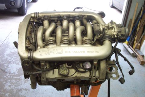 1995 Ford Taurus - A V6 engine, identified as SHO 24 Valve DOHC, is displayed on an engine stand in a garage.