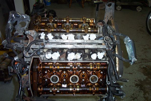 Engine with exposed camshafts and valves, covered in oil, with white cloths stuffed into cylinders