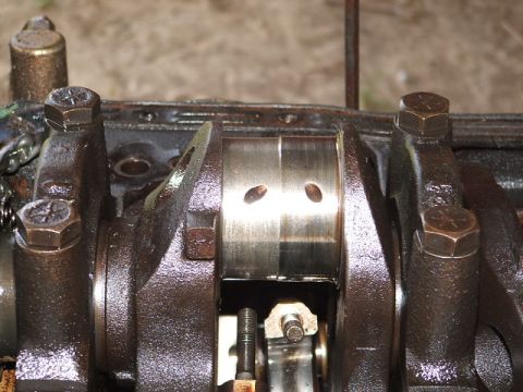 1966 Ford Ranchero - Close-up inside an oily engine block showing a polished crankshaft main journal with two oil holes, flanked by counterweights and dark cast…