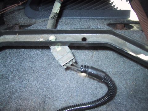 1994 Ford Bronco - Interior floor close-up showing a gray multi-pin electrical connector plugged together beneath a black seat frame rail, with split-loom con…