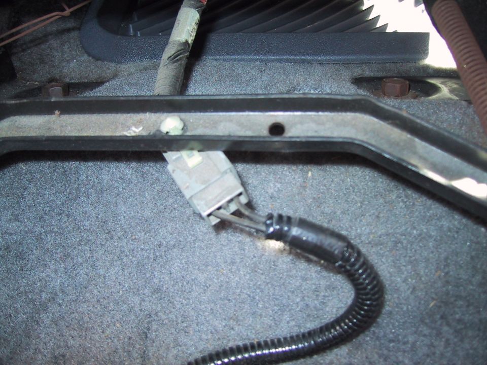 Gray multi-pin wiring connector and split-loom harness under seat rail on gray carpet