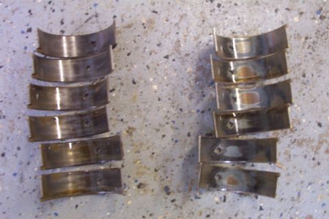 1995 Ford Taurus - Used engine bearing shells are laid out in two separate stacks on a speckled concrete surface.