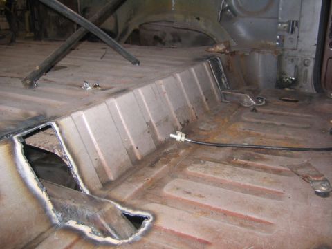1982 Ford Bronco - The interior floor of a vehicle shows signs of rust and modifications, with a visible cable running across.