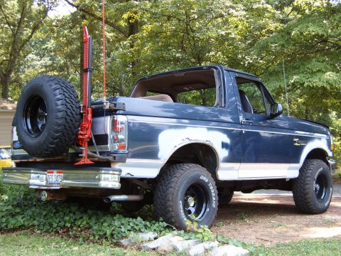 1993 Ford Bronco - This Ford Bronco has a spare tire and a Hi-Lift jack mounted on the rear bumper. The body shows primer on some panels.