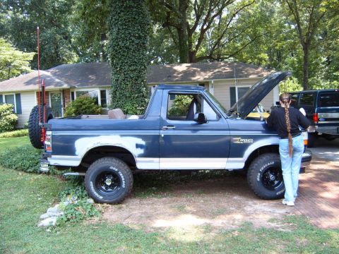1993 Ford Bronco - A blue Ford Bronco with its hood up is parked in a driveway next to another vehicle.