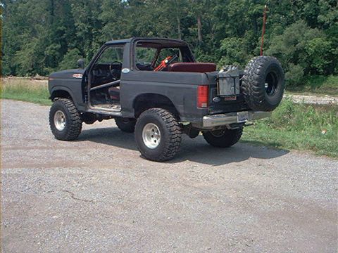 1986 Ford Bronco - This modified Ford Bronco is shown from the rear three-quarter view, with its doors off and a spare tire mounted externally.