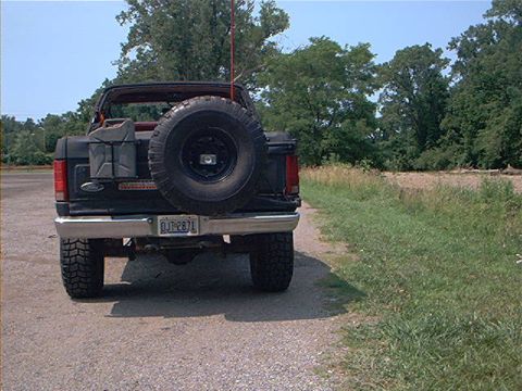 1986 Ford Bronco - Rear view of a black Ford Bronco with a spare tire and gas cans mounted on the back.