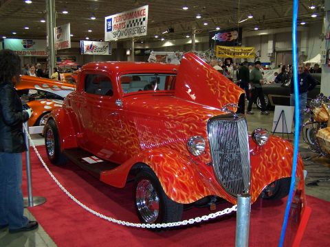 1995 Ford Probe - A vibrant red hot rod with custom flame graphics is showcased with its hood open at an indoor car show.