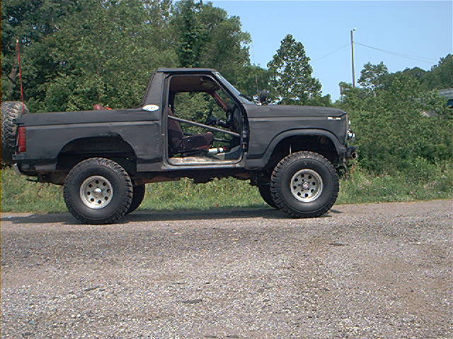 Dark SUV with roll cage, spare tire on rear, and off-road tires parked on a gravel road