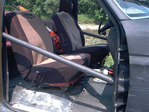 1986 Ford Bronco - The interior of a vehicle shows custom seat covers and a roll cage, with a body of water visible in the background.