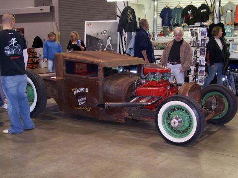 1995 Ford Probe - A custom-built rat rod pickup truck with a prominent red engine and distinctive green wire wheels is displayed indoors.