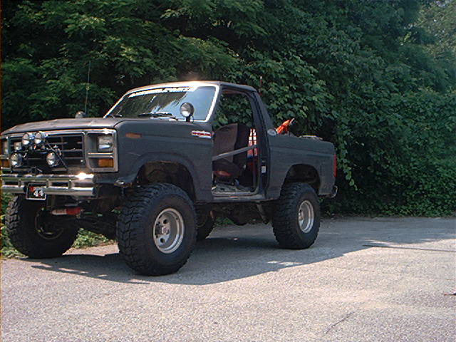 Modified dark gray Ford Bronco with off-road tires, roll cage, and aftermarket lights