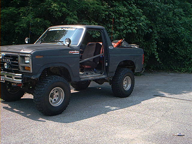 Dark gray SUV with off-road tires, roll cage, and no doors parked on asphalt