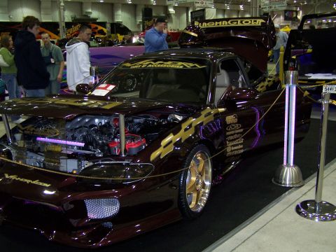 1995 Ford Probe - A highly customized coupe is displayed indoors with its engine exposed and adorned with gold racing stripes and decals.