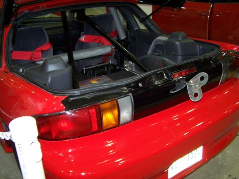 1995 Ford Probe - Rear view of a red car's interior, modified with a roll cage and racing seats, and a wind-up toy key attached to the trunk.
