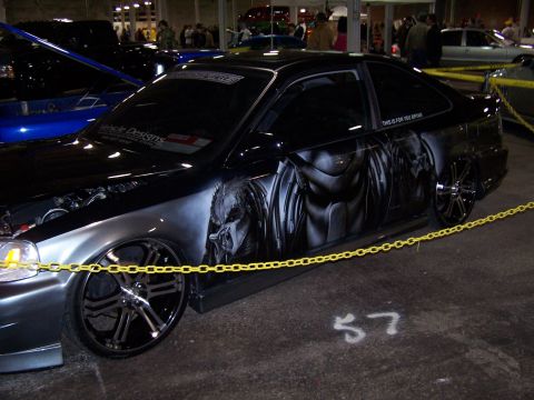 1995 Ford Probe - A customized coupe with airbrushed predator graphics is displayed indoors, with other vehicles and people in the background.