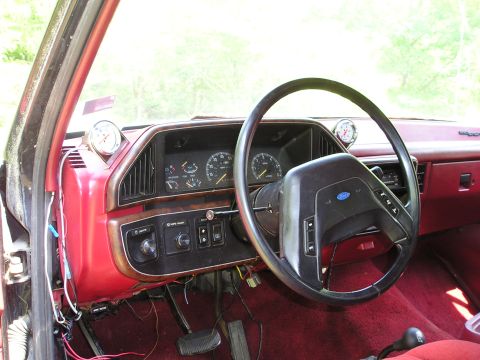 1988 Ford Bronco - The interior of a vehicle shows the dashboard, steering wheel, and carpeting, with added gauges on the dash.