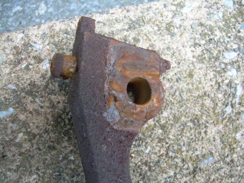 1988 Ford Bronco - A heavily rusted metal bracket with a bolt is shown close-up against a concrete surface.