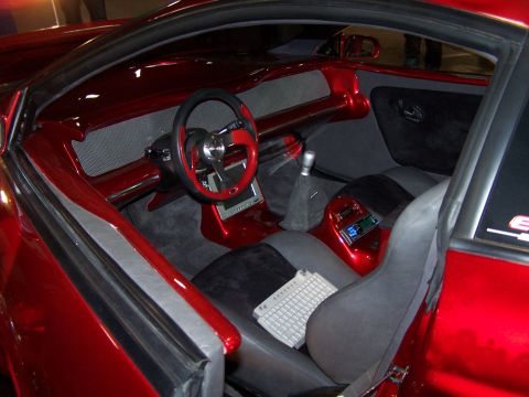1995 Ford Probe - The interior of a modified red car shows a custom dashboard, a unique steering wheel, and a keyboard placed on the passenger seat.