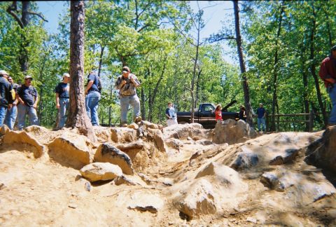 1988 Ford Bronco - A group of people observe a pickup truck navigating a rocky off-road trail in a wooded environment.