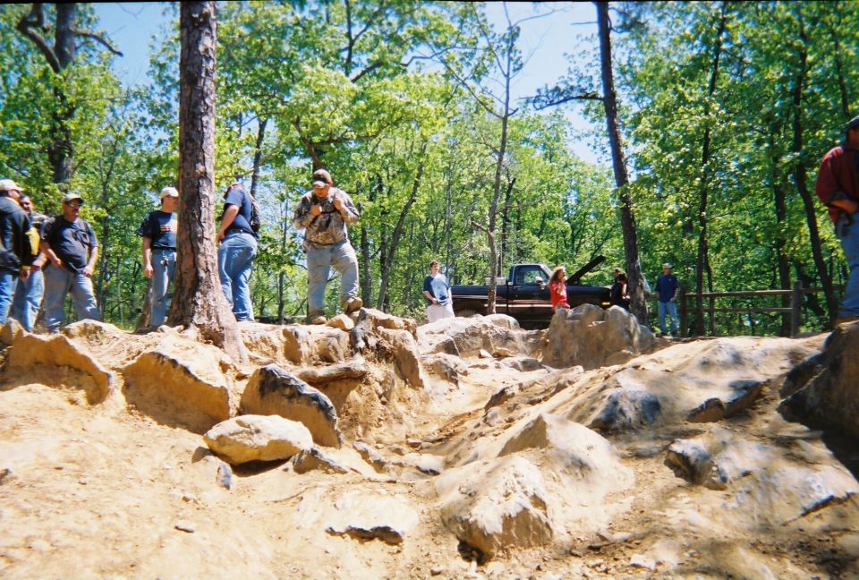 Off-road scene with a pickup truck and people gathered in a wooded area